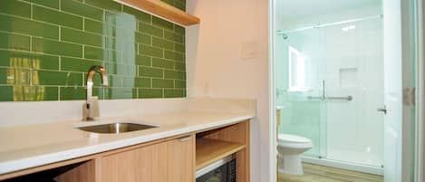 Een moderne badkamer met een glazen douchecabine, een toilet en een wastafel met een groene tegelachtergrond.