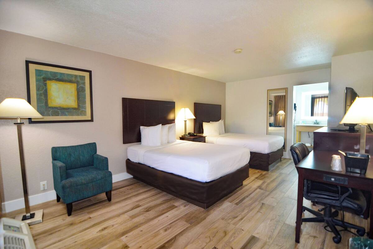 A hotel room with two beds, a desk, a chair, and a lamp.