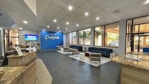 A reception area with a large blue wall displaying 'Orlando' and a seating area with sofas and a coffee table. - Hotel Monreale Inn & Studios I-Drive Icon Park Orlando (Orlando)