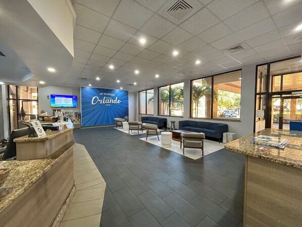 A reception area with a large blue wall displaying 'Orlando' and a seating area with sofas and a coffee table. - Hotel Monreale Inn & Studios I-Drive Icon Park Orlando (Orlando)