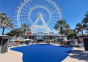 A large Ferris wheel with a blue floor in the foreground, surrounded by palm trees and various shops. - Hotel Monreale Inn & Studios I-Drive Icon Park Orlando (Orlando)