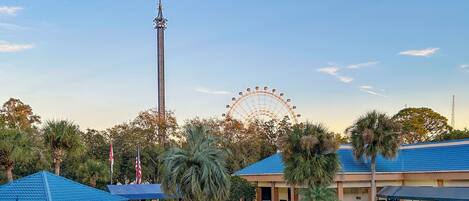 A pool area with lounge chairs, a Ferris wheel, and a tall tower in the background.