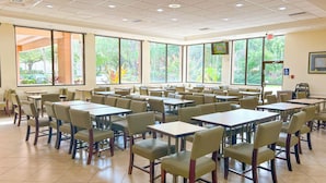 A spacious indoor area with multiple tables and chairs, large windows with a view of greenery, and an exit sign on the wall. - Hotel Monreale Inn & Studios I-Drive Icon Park Orlando (Orlando)