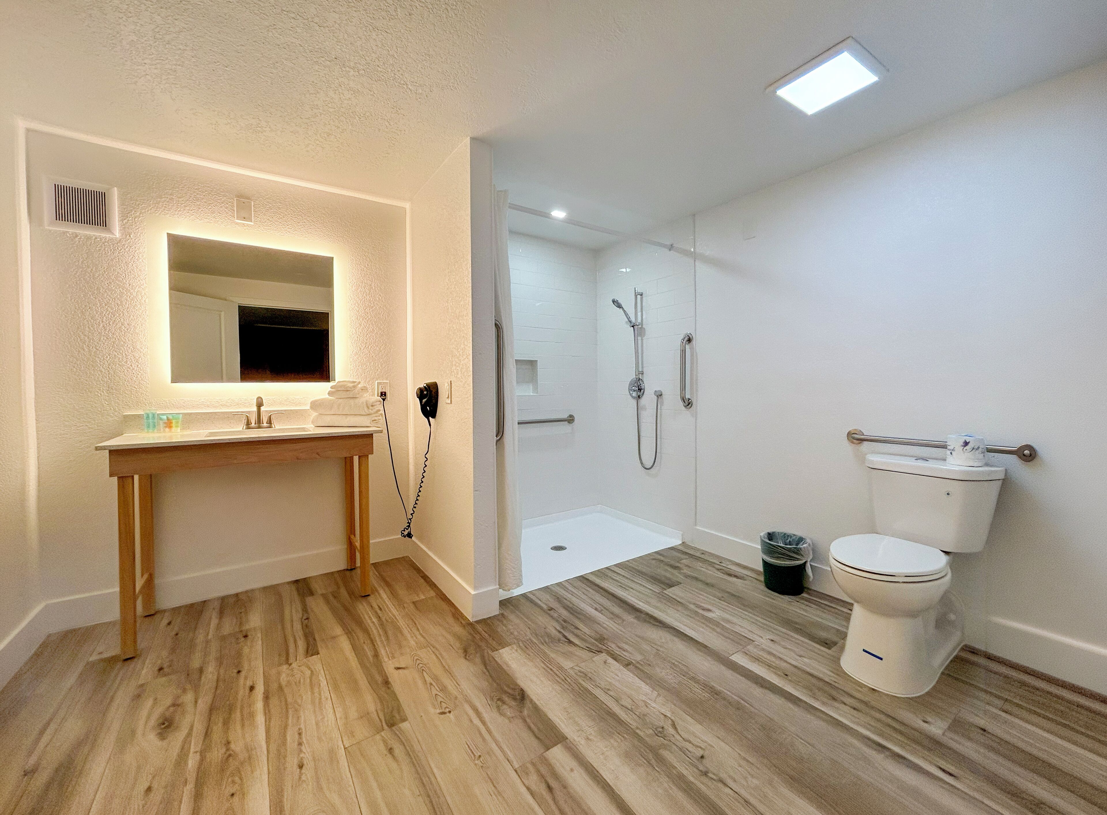 A bathroom with a wooden vanity, a mirror, a shower, and a toilet.