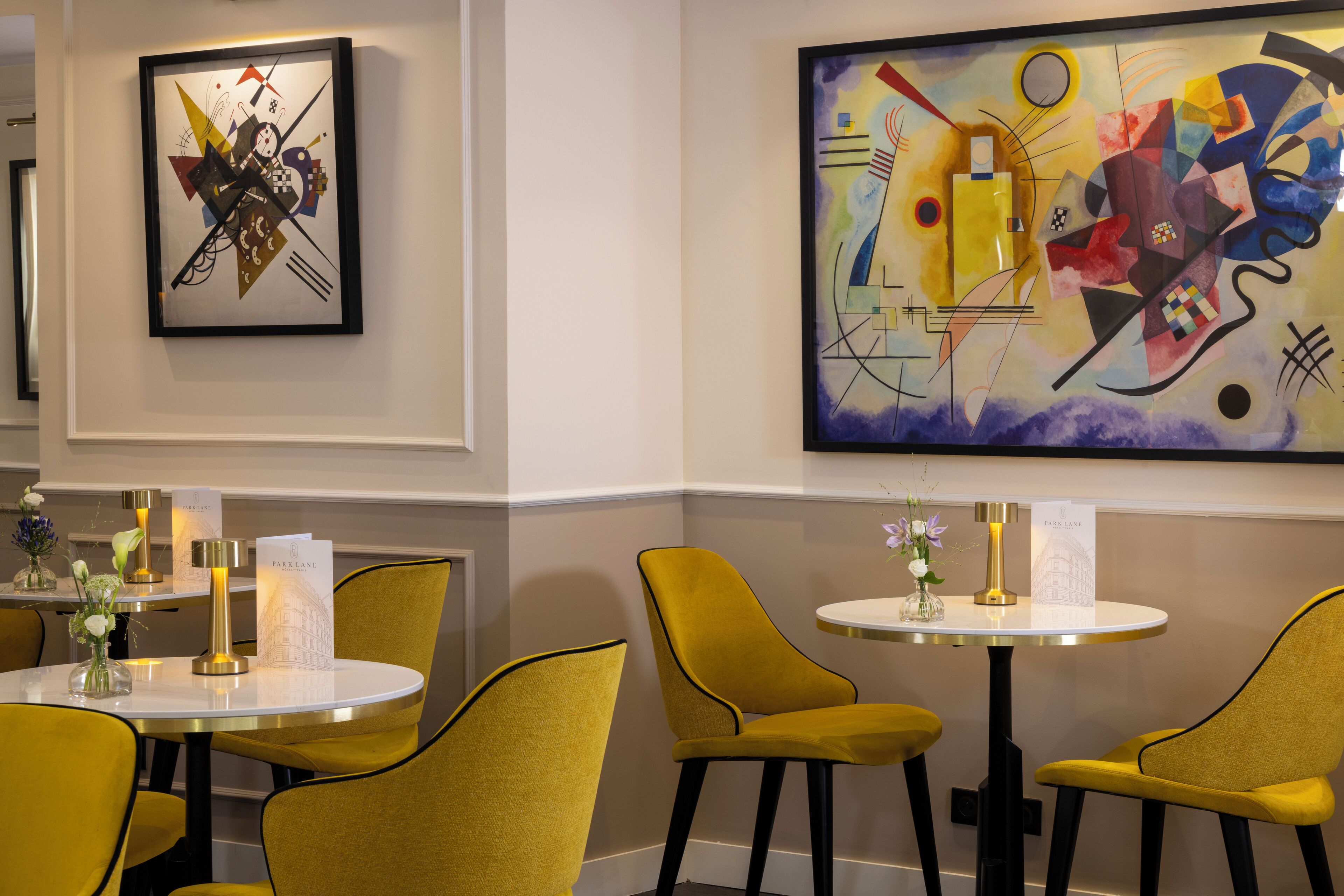 A dining area with yellow chairs and round tables, featuring abstract art on the walls.