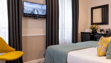 Hotellihuone, jossa on sänky, seinälle asennettu televisio, työpöytä, jossa on kahvinkeitin, ja tuoli.