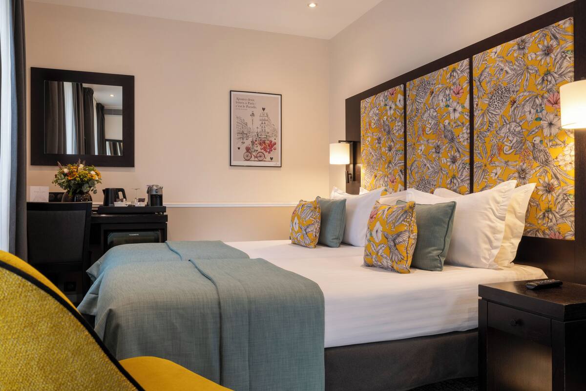 A hotel room with a large bed, a desk with a chair, a mirror, and a wall with a floral pattern.
