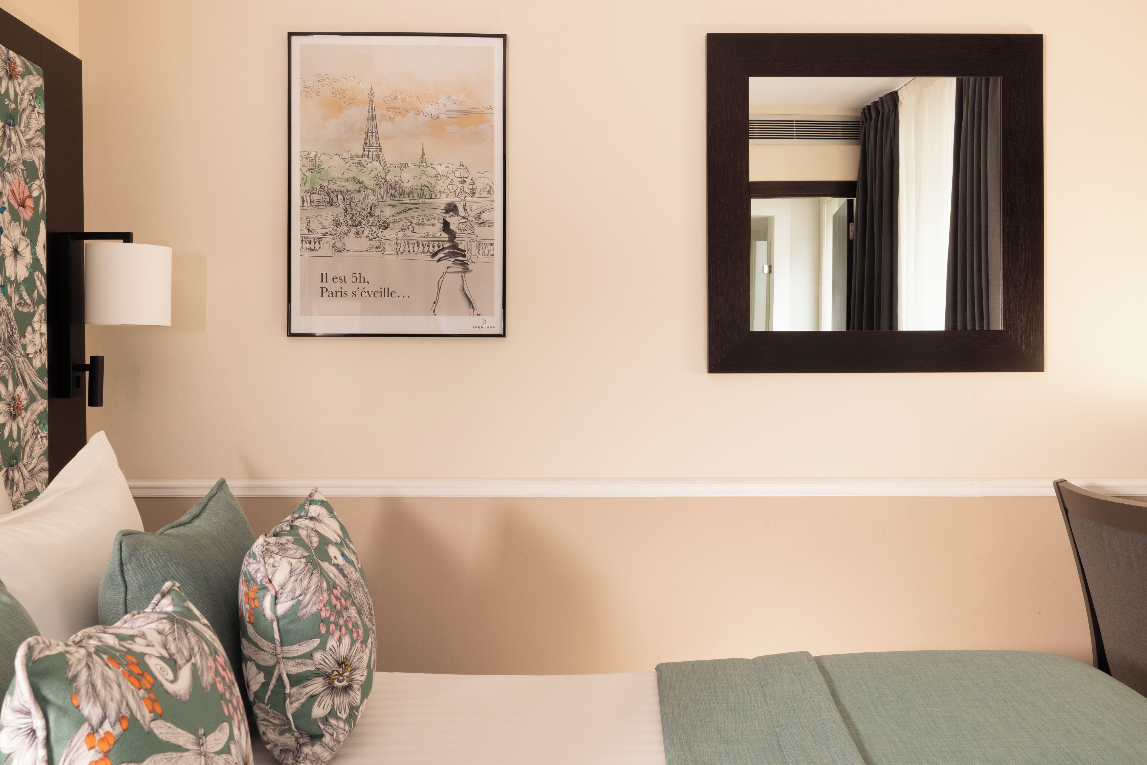 Ein Hotelzimmer mit einem Bett, Kissen mit Blumenmuster, einem gerahmten Bild von Paris, einem Spiegel und einer Lampe.