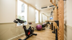 A gym with exercise equipment, a large window, and a wooden wall. - Hotel Park Lane Paris (Paris)