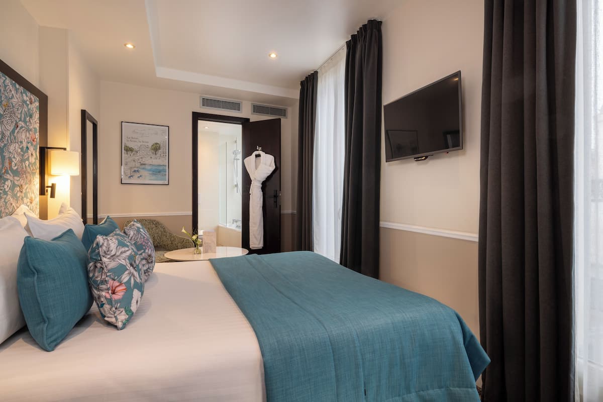 A hotel room with a large bed, a flat-screen TV, a bathroom with a shower, and a painting on the wall.