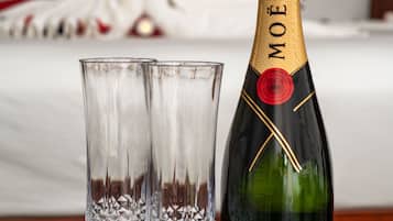 A bottle of Moët & Chandon champagne and two crystal glasses on a table with a red flower, in a hotel room with a bed and heart-shaped decoration in the background.