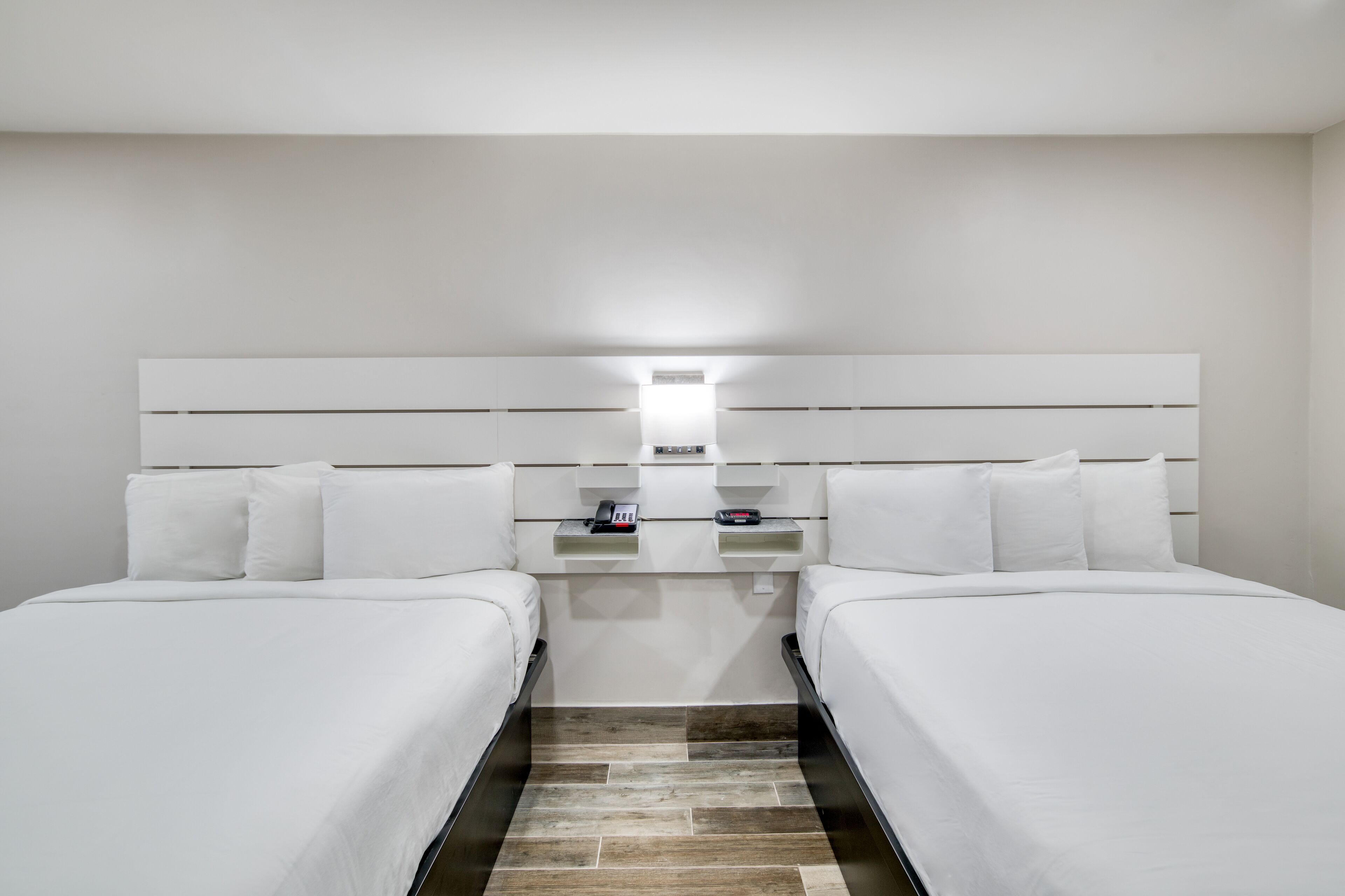 Habitación de hotel con dos camas individuales, una mesita de noche con teléfono y cabecero con iluminación integrada.