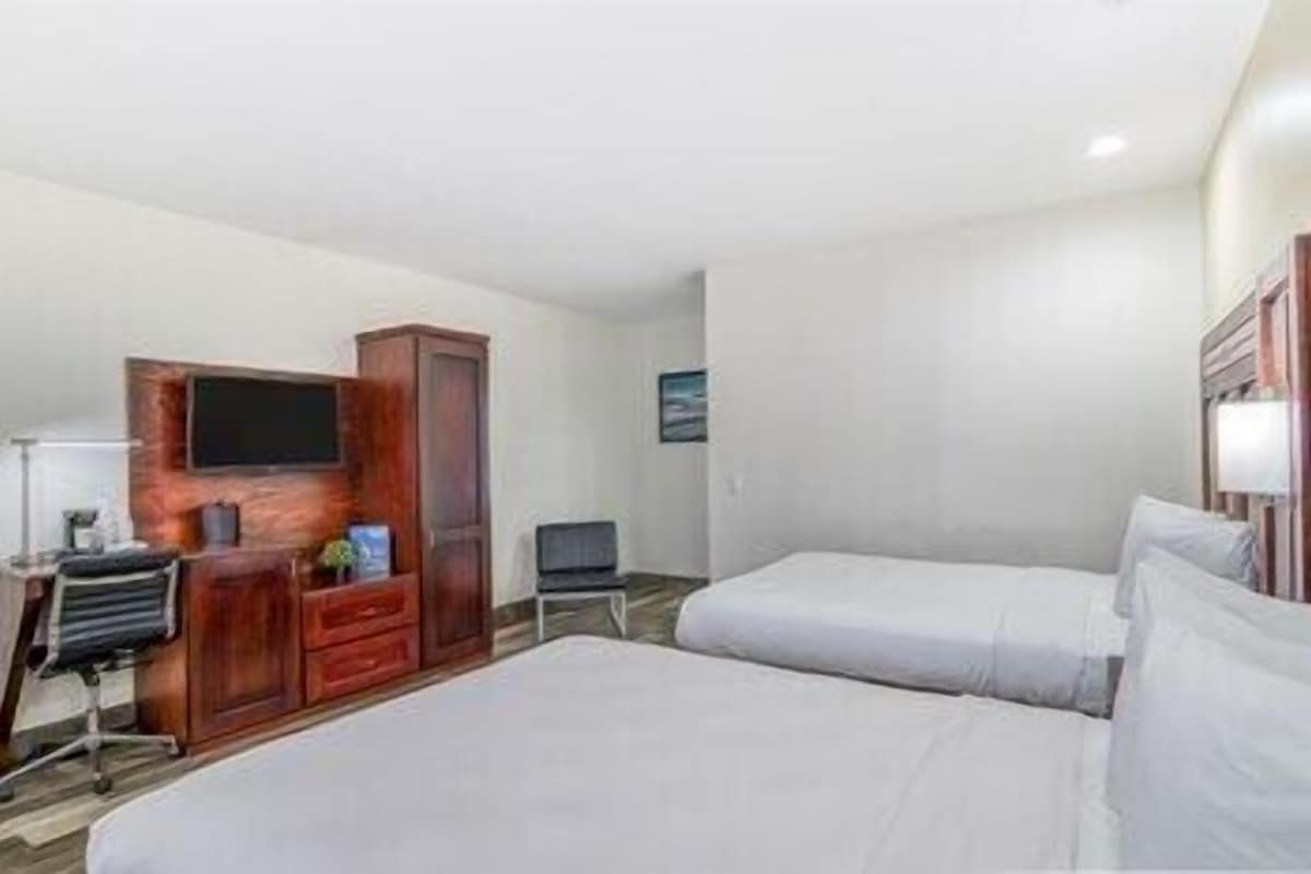A hotel room with two beds, a TV, a desk with a chair, and a wardrobe.