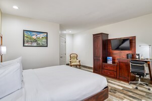 A hotel room with a bed, a wooden desk with a TV, a chair, and a wardrobe.