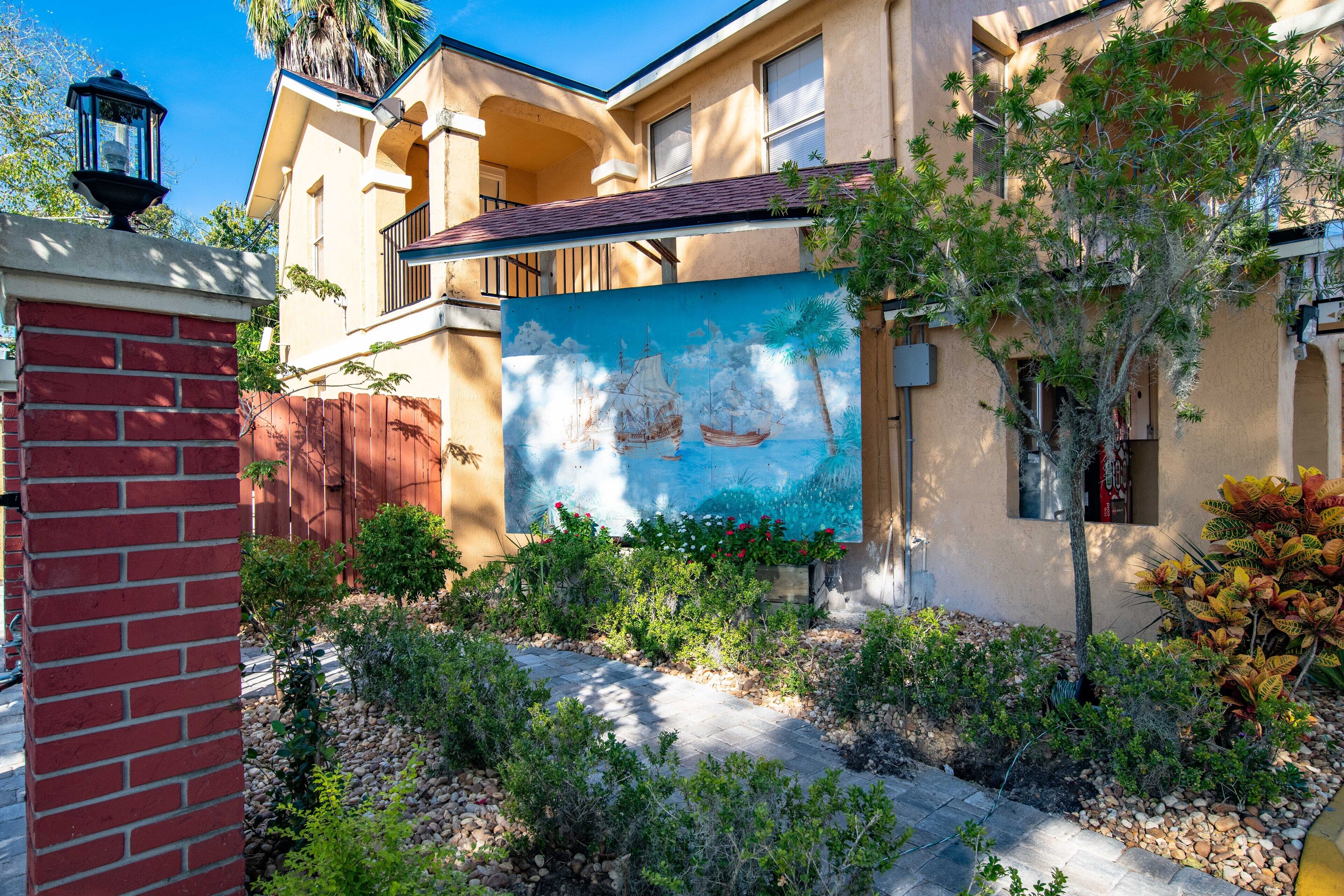 A building with a mural of a sailing ship, a brick wall, and a landscaped garden with various plants.