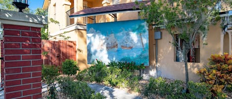 A building with a mural of a sailing ship, a brick wall, and a landscaped garden with various plants.
