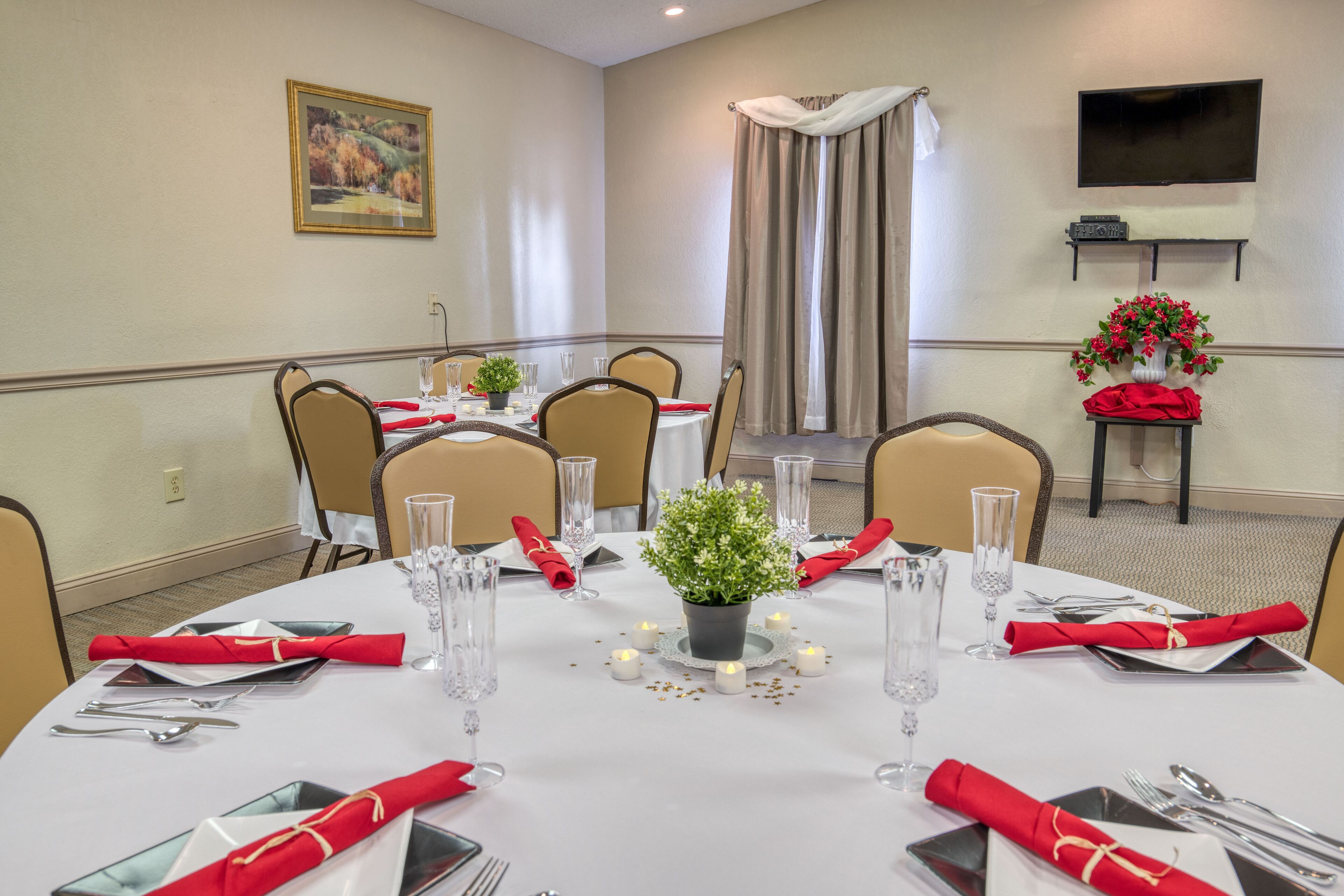 Un salón de conferencias con mesas redondas dispuestas para comedor, equipado con sillas, copas y servilletas rojas.