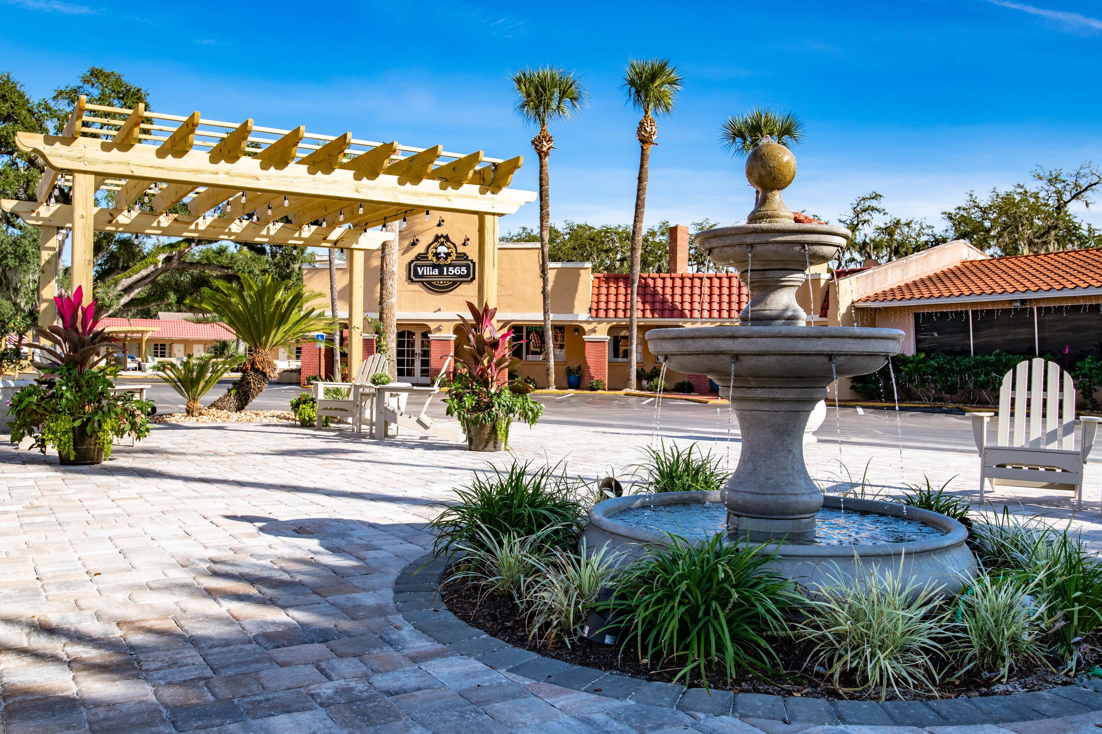 A courtyard with a fountain, palm trees, and a wooden pergola with a sign.