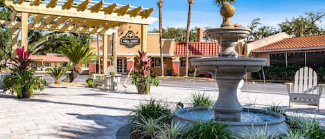 A courtyard with a fountain, palm trees, and a wooden pergola with a sign.