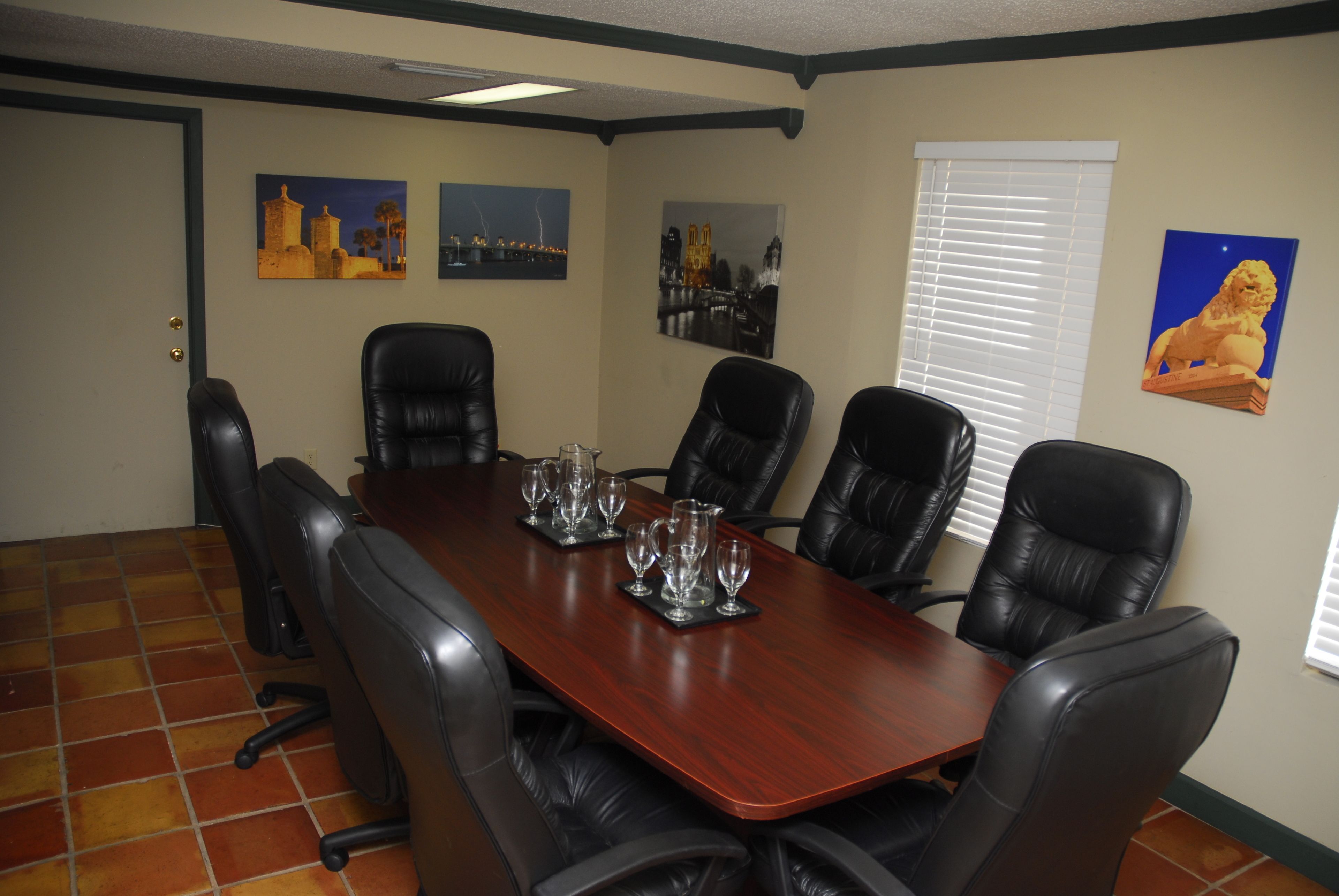 Un salón de conferencias con una mesa de madera, sillas de cuero negro y tres cuadros en las paredes.