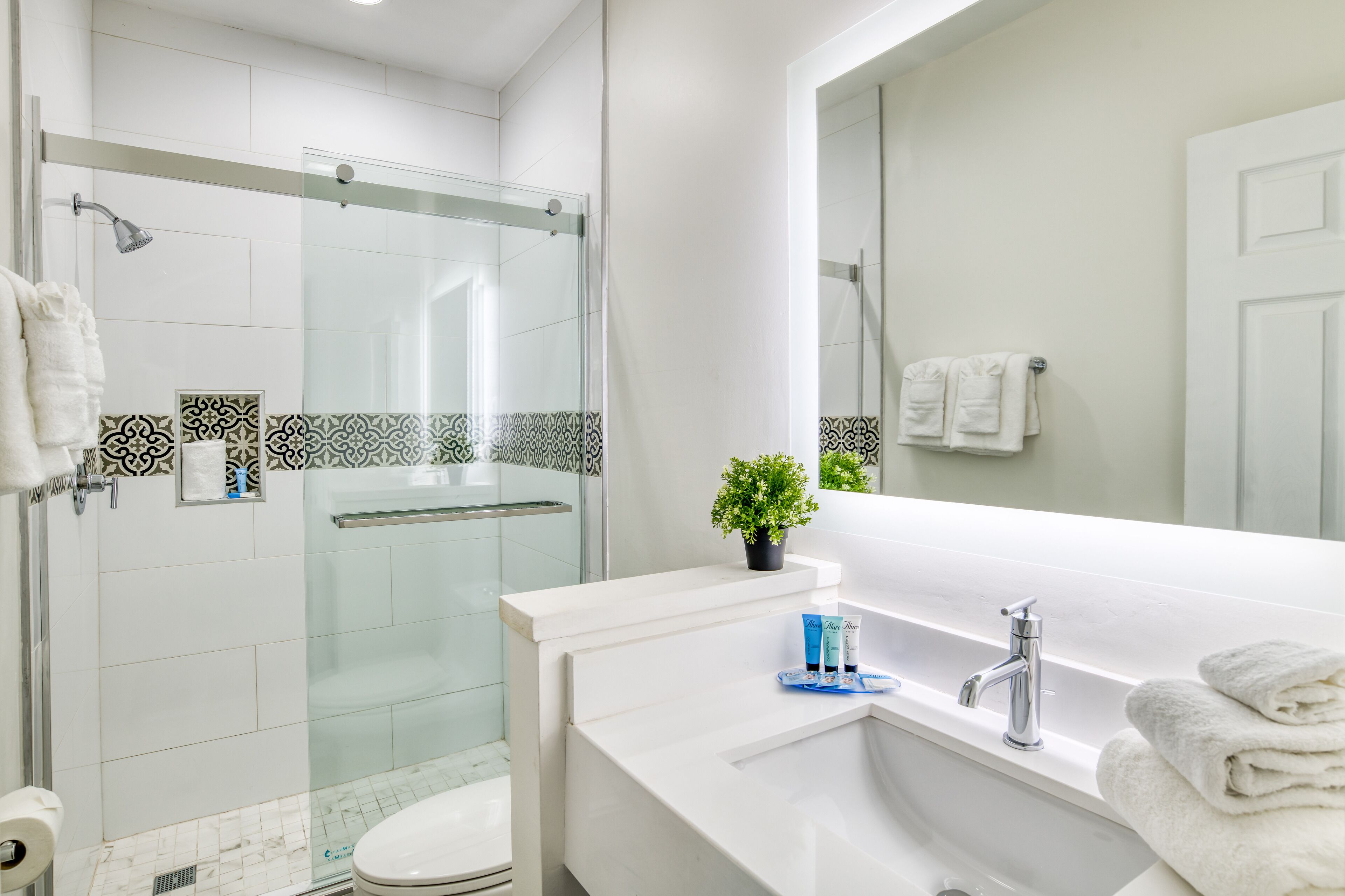 A modern bathroom with a glass-enclosed shower, a white sink with a mirror, and a toilet.