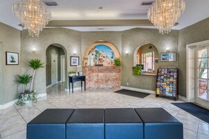 Una zona de recepción con piso de mármol, un mostrador de recepción, un banco azul y un panel informativo en la pared.