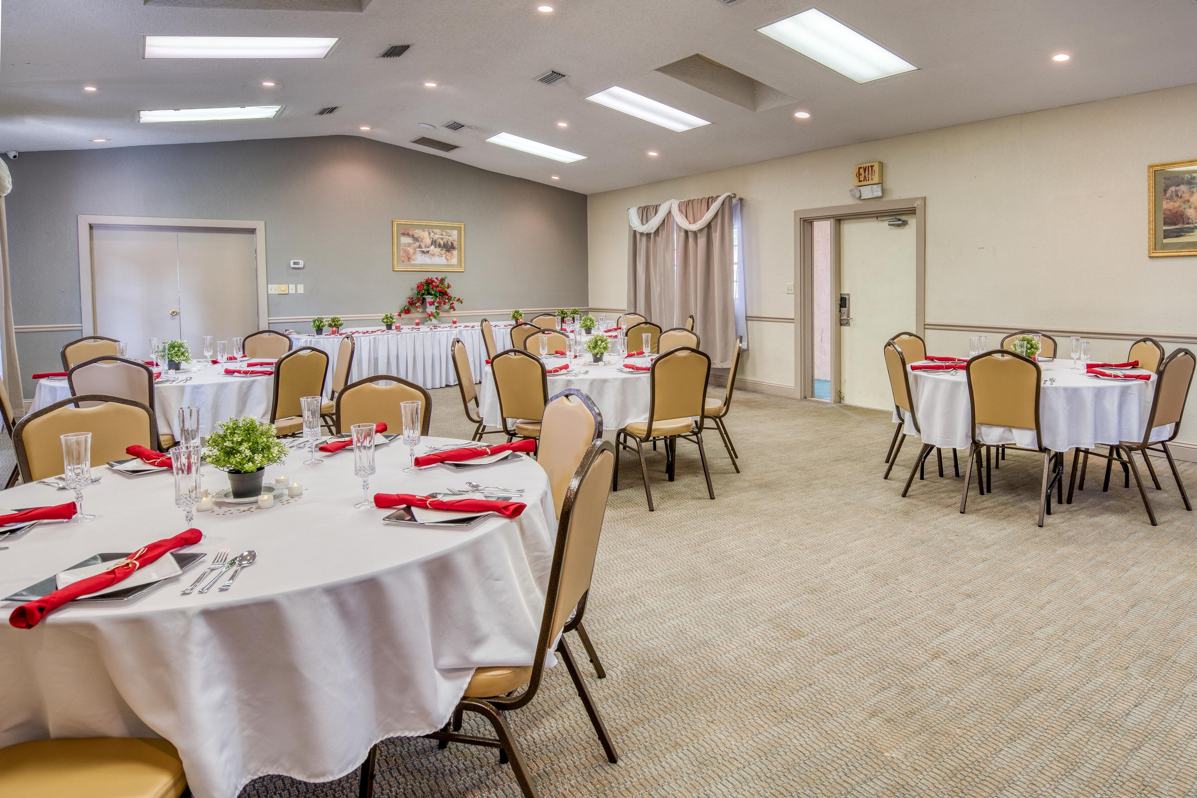 Un salón de conferencias con varias mesas redondas, cada una cubierta con manteles blancos, servilletas rojas y cristalería.