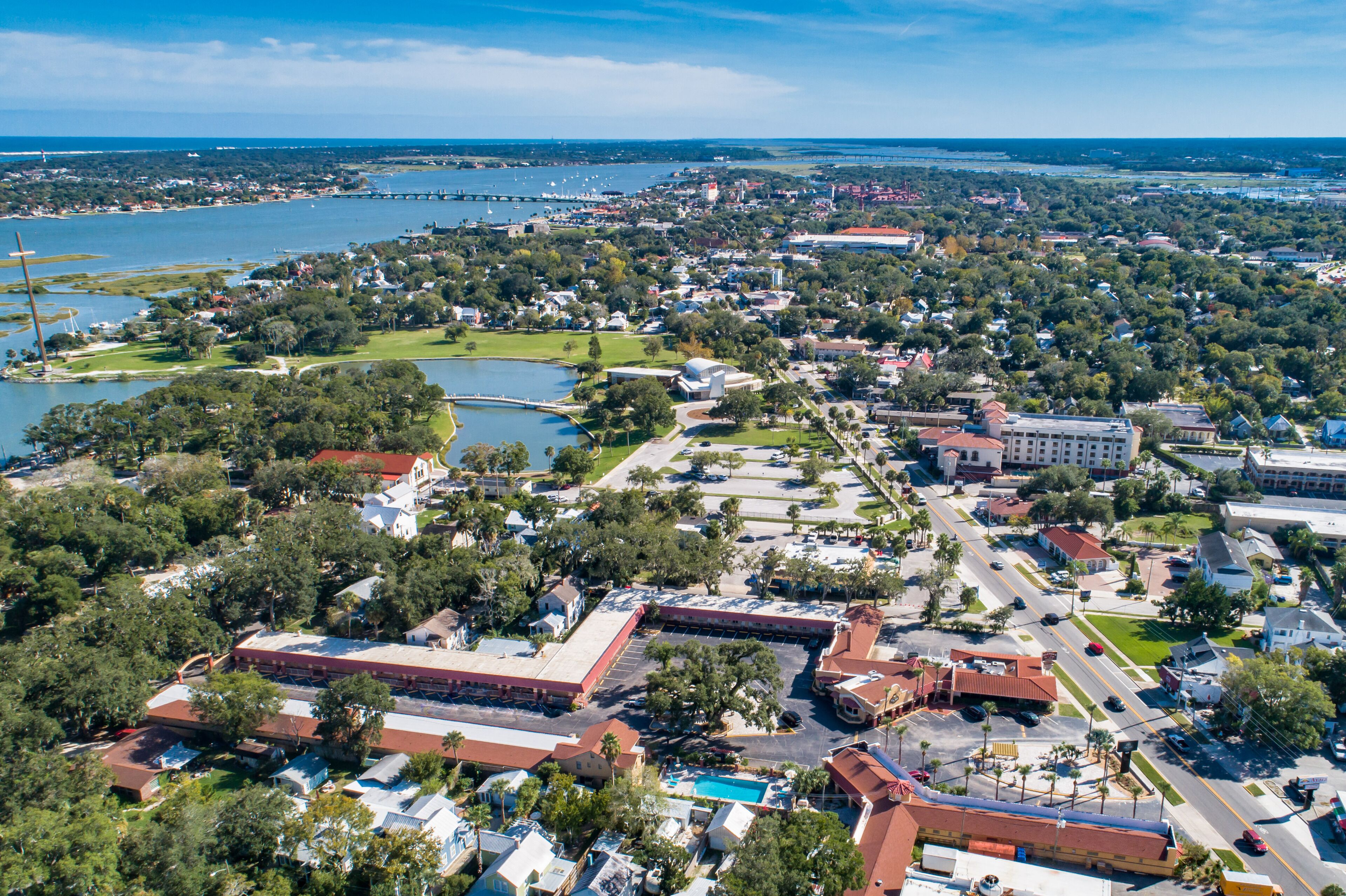 An aerial view of a coastal town with a marina, residential areas, and a large building with a red roof.