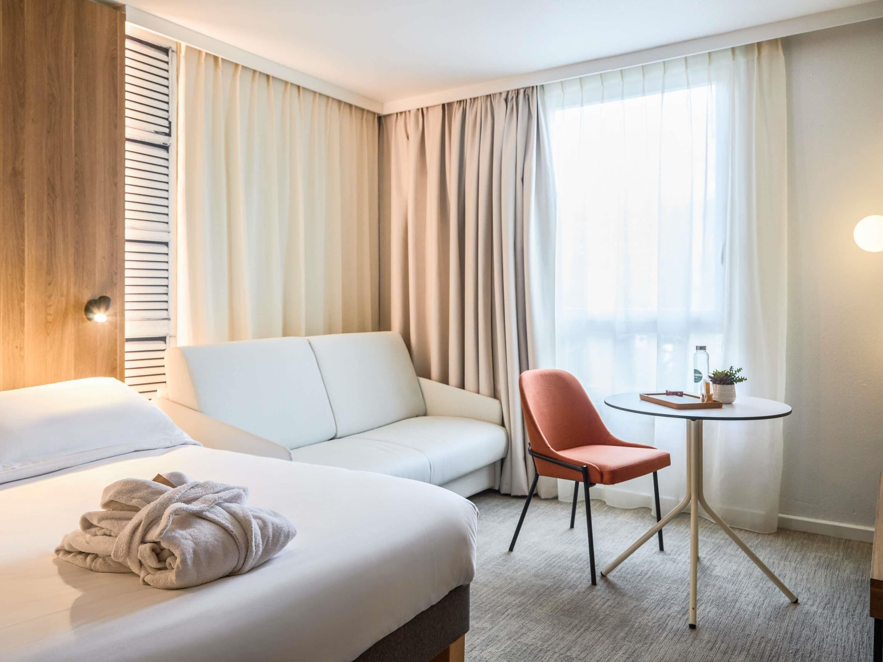 A hotel room with a bed, a sofa, a chair, a small table, and a window with curtains.