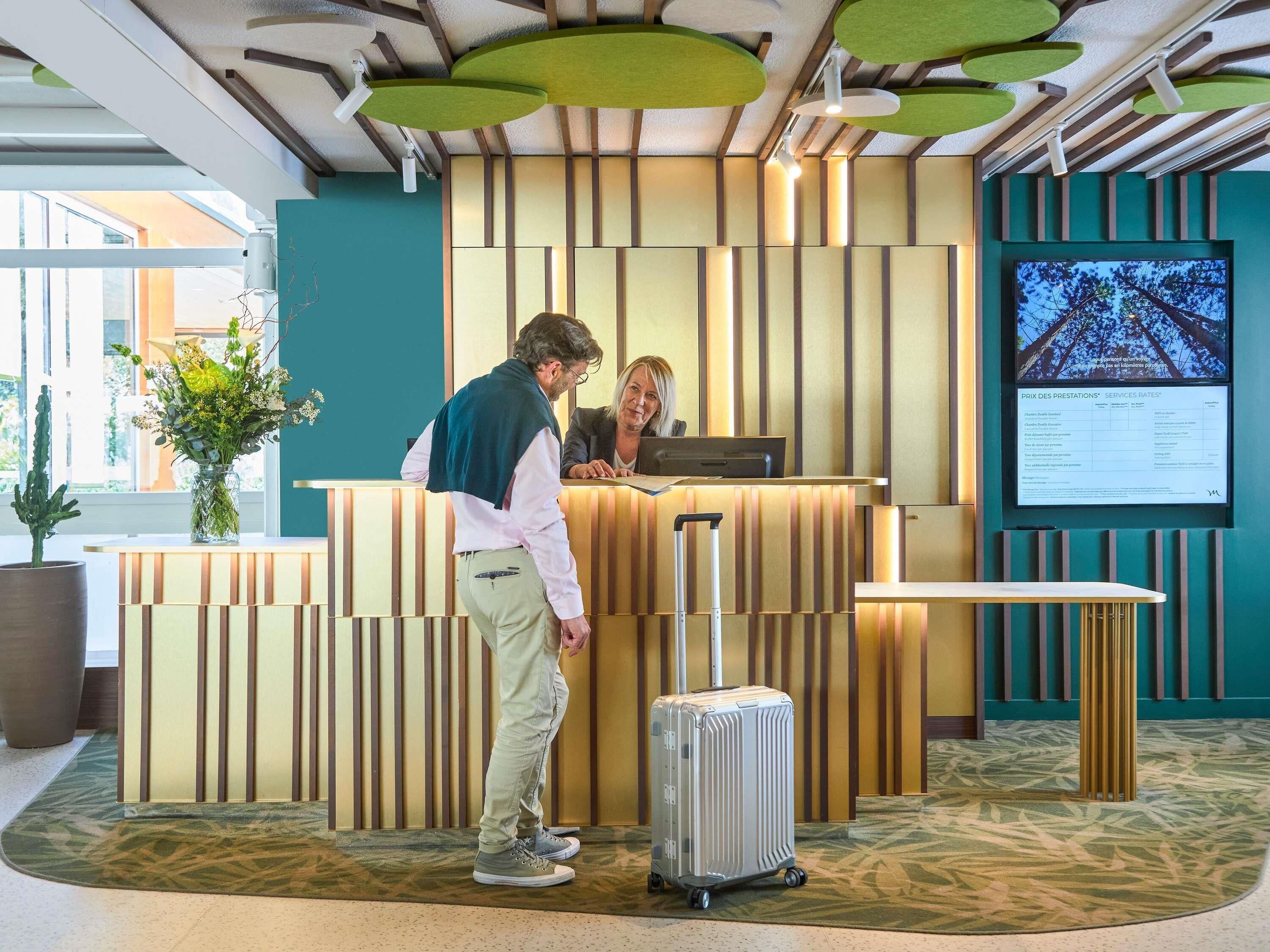 A reception area with a reception desk, a monitor displaying information, and a potted plant.