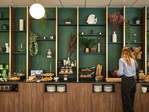 A person standing at a counter with various food items and a teddy bear on the shelves. - Mercure Aix en Provence Beaumanoir (Aix-en-Provence)