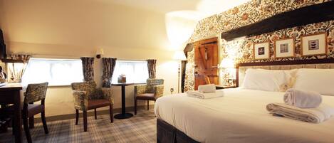 A hotel room with a large bed, a dining table with chairs, a small table with a lamp, and a window with curtains.