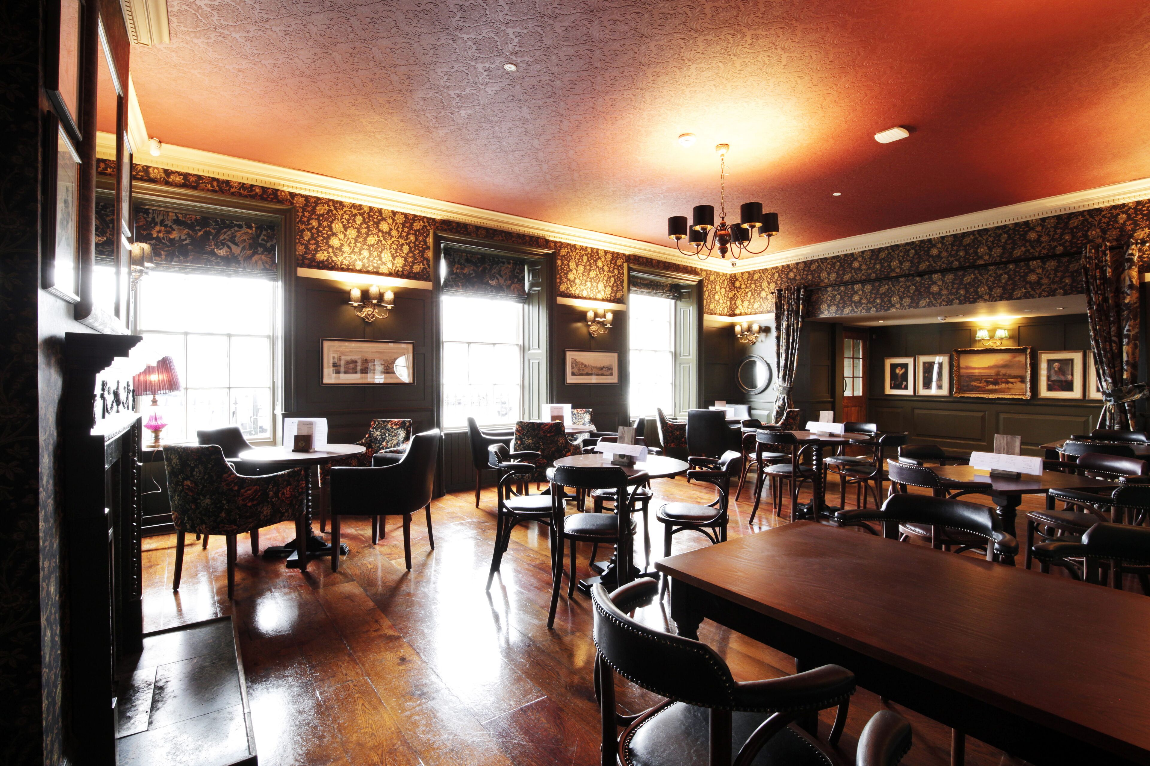 A restaurant with a classic interior, featuring wooden tables and chairs, framed pictures on the walls, and a chandelier.