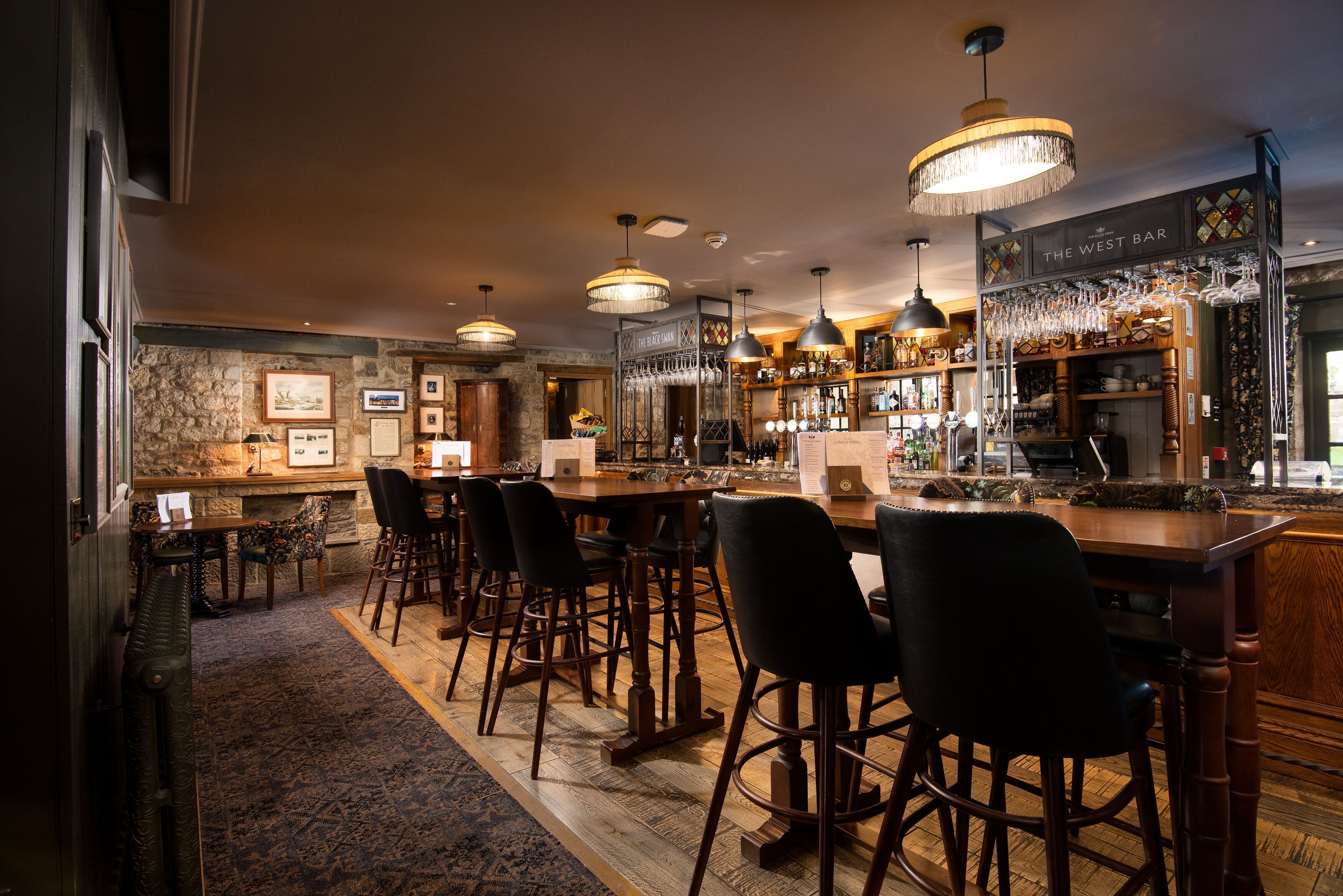 A bar area with wooden furniture, hanging lights, and a stone wall.