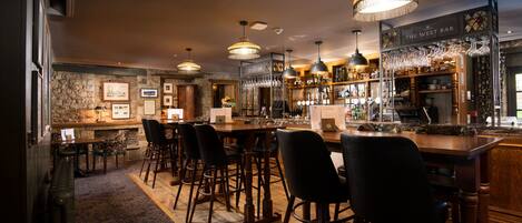 A bar area with wooden furniture, hanging lights, and a stone wall.