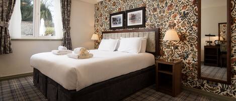 A neatly made bed with white linens, a dark headboard, and a plaid carpet. There are two bedside lamps and a mirror on the wall.