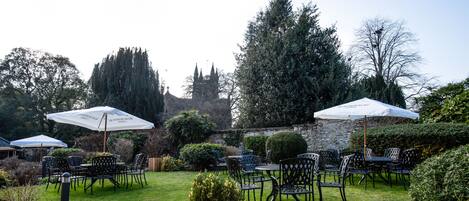 An outdoor patio with tables and chairs, surrounded by stone walls and greenery.
