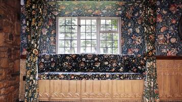 Una habitación con un ventanal grande, papel tapiz floral y un banco de madera.