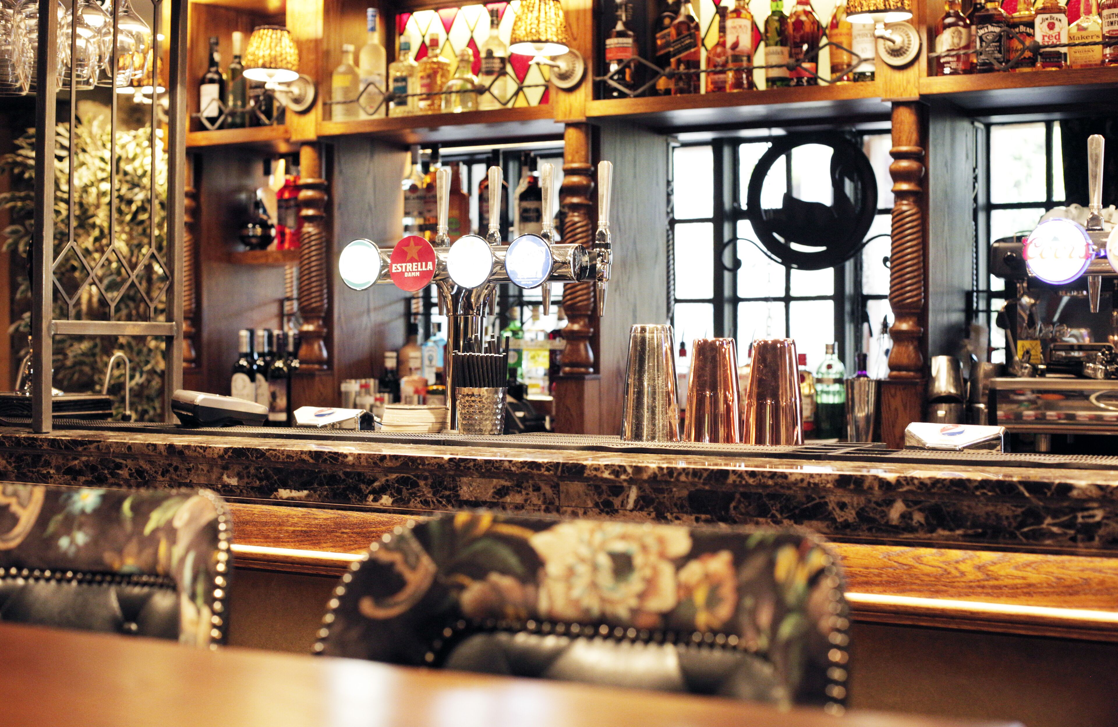 A bar area with a marble countertop, multiple taps, and a variety of bottles and glasses.