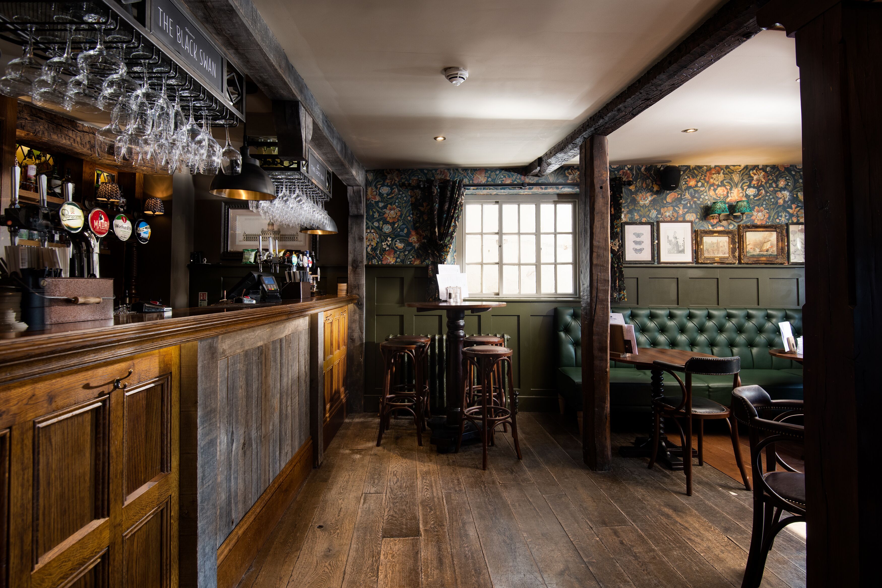 Eine Bar mit Holzboden, einer Bar mit mehreren Zapfhähnen und einer gepolsterten grünen Sitzecke.