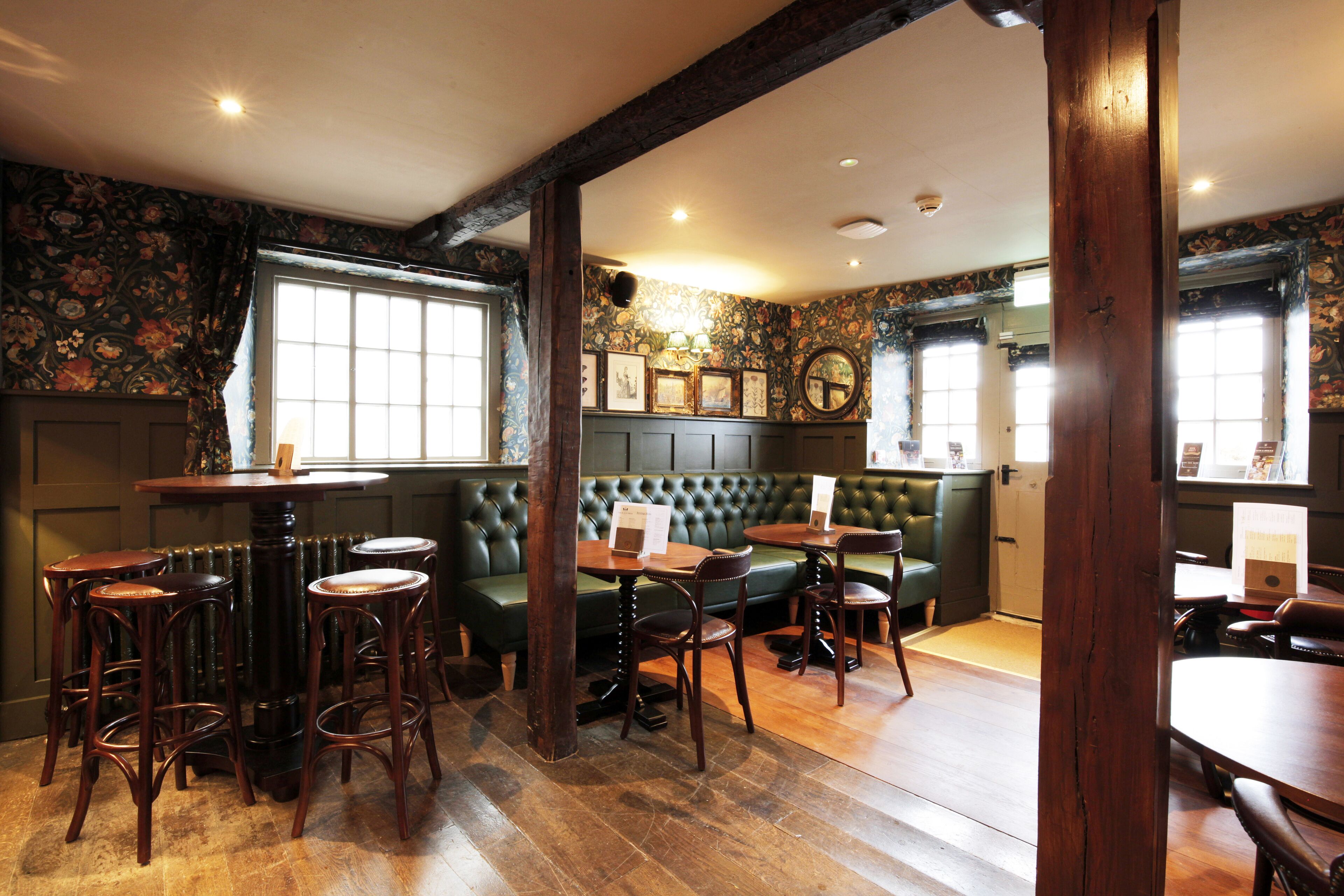 A restaurant interior with wooden tables, green cushioned seating, and a fireplace.