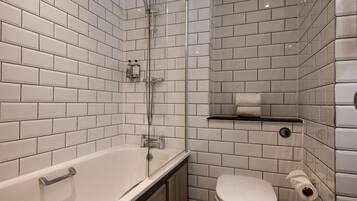 Un bagno moderno con piastrelle bianche stile metro, una doccia con pareti in vetro, una vasca da bagno bianca e un water con portarotolo.