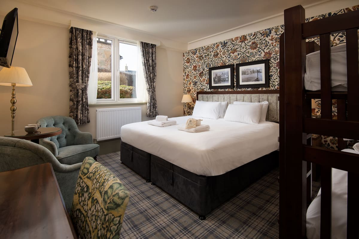 A hotel room with a large bed, a chair, a table, and a window with curtains.