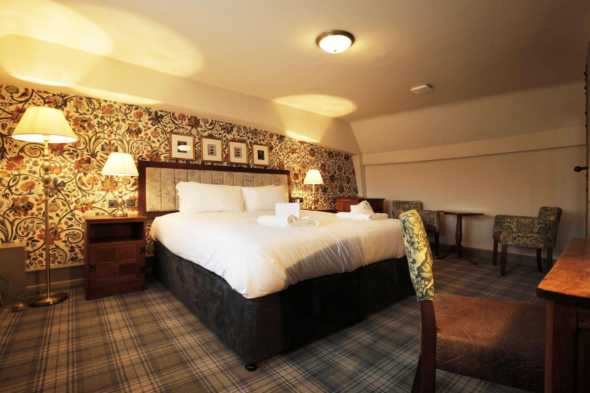 A hotel room with a large bed, two bedside tables, a chair, a small table, and a patterned wallpaper.