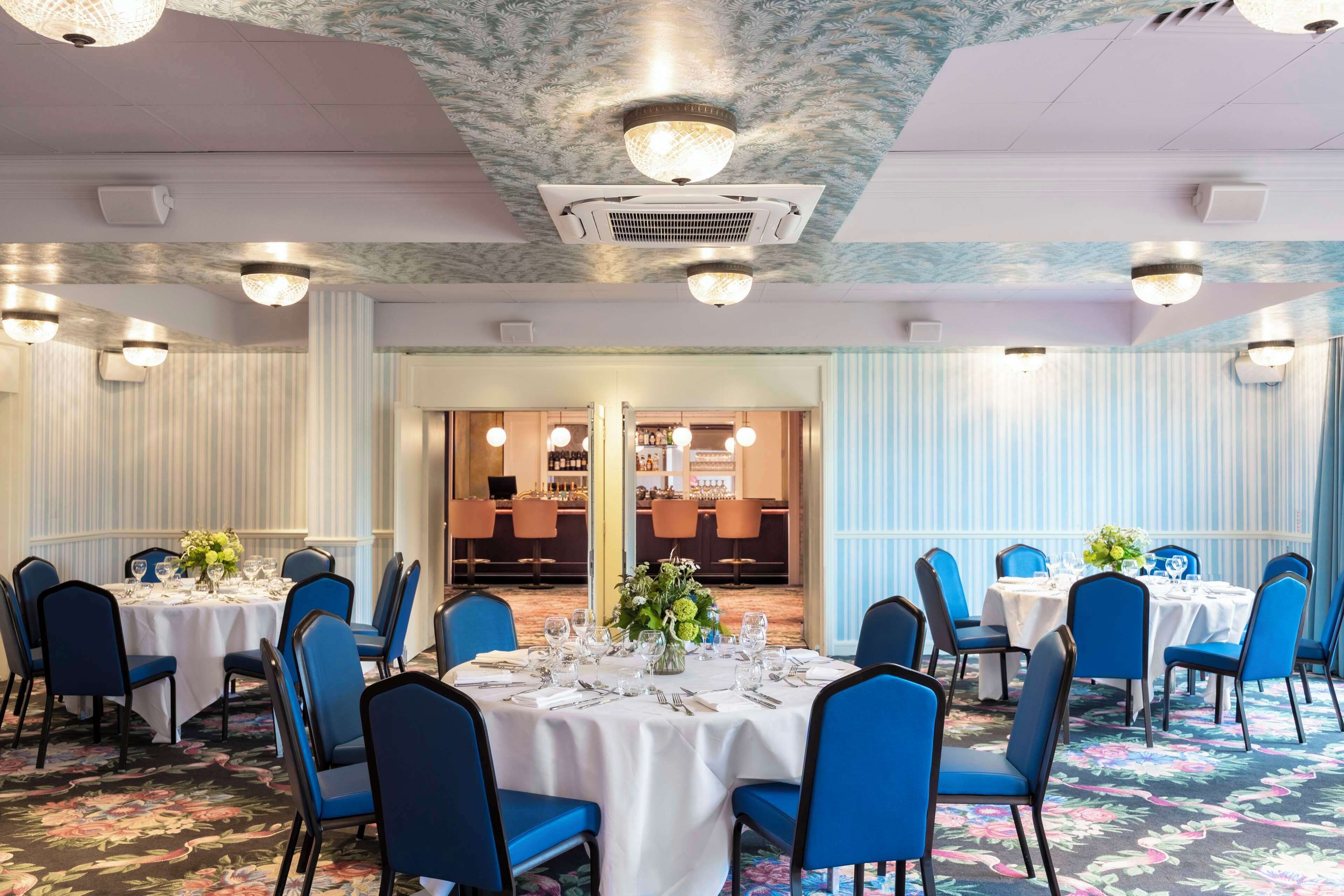 A banquet hall with round tables, blue chairs, and white tablecloths.