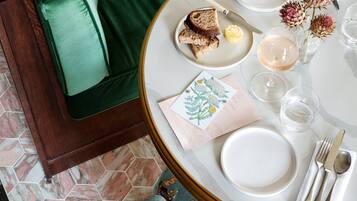 Una mesa de comedor dispuesta con platos, cubiertos y una copa de vino, rodeada por un sofá verde y cojines con estampado floral.