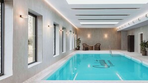 A modern indoor swimming pool with clear water, surrounded by large windows and contemporary lighting fixtures.