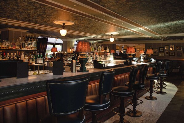 A bar area with leather bar stools, a well-stocked bar counter, and ambient lighting.