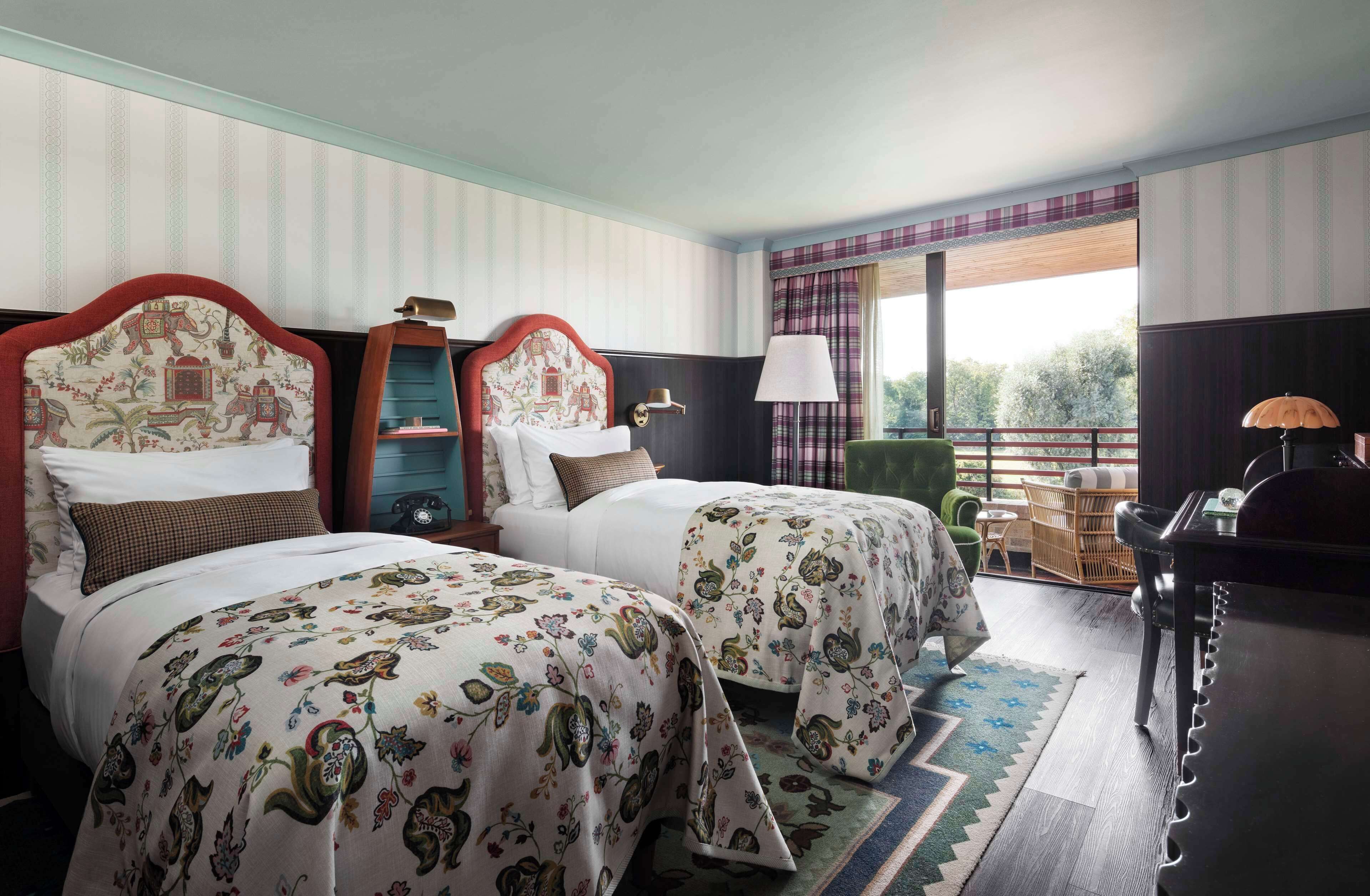 Habitación de hotel con dos camas, un escritorio, una silla y vistas al exterior.