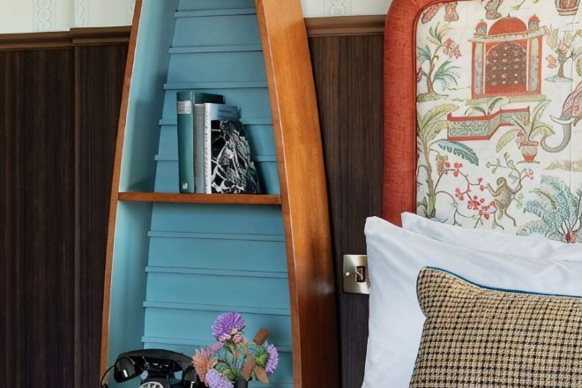A room with a wooden ladder, a shelf with books and decorative items, a patterned pillow, and a bed with a checkered pillow.